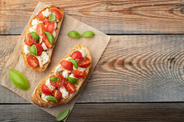 Bruschetta with tomatoes, mozzarella cheese and basil on a old rustic table. Traditional italian appetizer or snack, antipasto. Top view with copy space. Flat lay