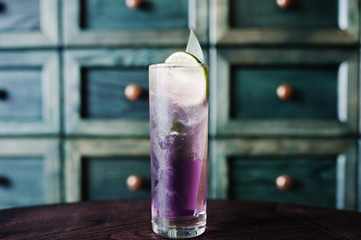 Alcoholic long violet cocktail with ice in glass at bar table.