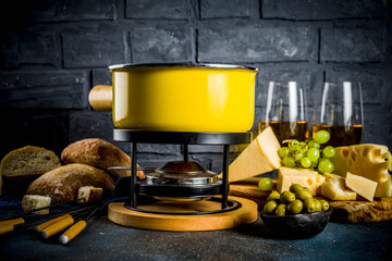 Gourmet Swiss fondue in traditional fondue pot, with forks, various cheeses, olives, bread and...