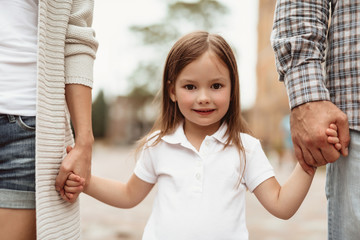 Waist up portrait of small smiling girl standing and holding mother and father hands. She is happy...