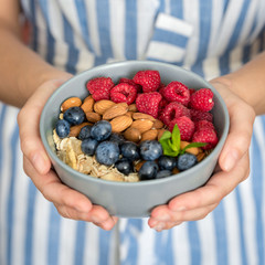 Eating healthy breakfast bowl. Yogurt, granola, seeds, fresh and dry fruits and honey in gray ceramic bowl in woman's hands. Clean eating, dieting, detox, vegetarian food concept