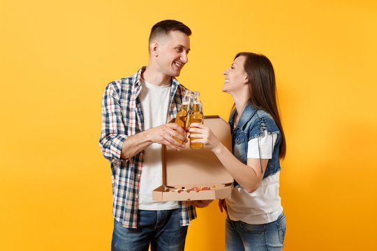 Young smiling couple woman and man sport fans cheer up support team clinking beer bottles hold italian pizza in cardboard flatbox isolated on yellow background. Sport family leisure lifestyle concept.