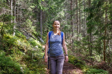 Young smiling woman with backpack hiking in mountain forest