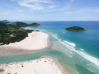  Aerial view of Brazilian beach with blue sky, white clouds, tourists in the sand, green and blue sea.