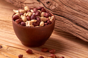 Deep fried peanuts in clay bowl over rustic wooden background. Selective focus