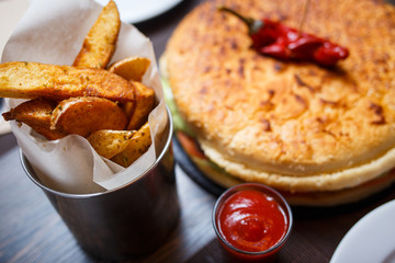 Golden potato wedges with big burger on the table in a restaurant. Close-up top view