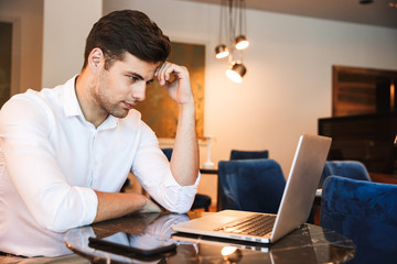 Pensive young formal dressed man working on laptop