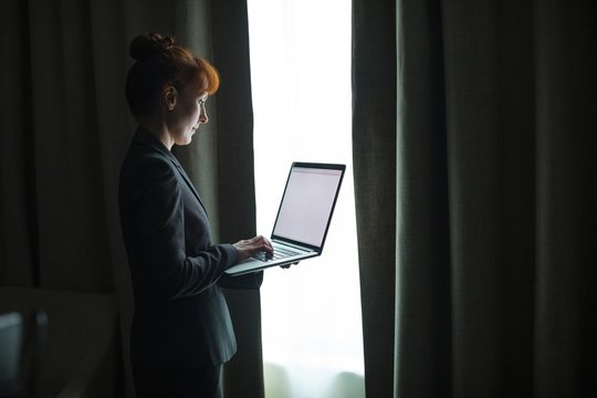 Side view of businesswoman working on laptop while standing indoors