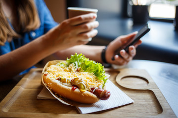Young woman having hot dog with coffee for lunch in cafe.