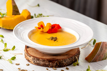 Ukrainian cuisine. Pumpkin puree soup, with cream, pumpkin seeds and flowers on a white plate. Copy space, selective focus