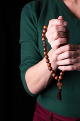 Rosary, cross   in female hands on a dark background. 