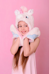 Caucasian beautiful little girl in a hat with  unikorn  on a pink background.