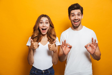 Photo of excited coup;e man and woman in basic clothing screaming and gesturing symbols with fingers at camera, isolated over yellow background