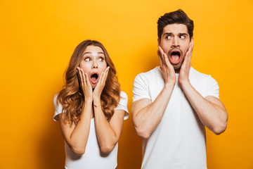 Image of shocked people man and woman in basic clothing expressing surprise or fright with open mouth covering face, isolated over yellow background
