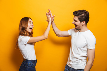 Image of friendly young people man and woman in basic clothing laughing and giving high five,...