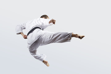 On a light background, an adult athlete with a black belt beats a kick in jump