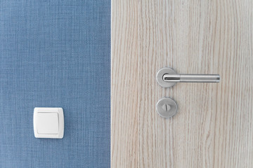 Door handle and inner lock on a wooden doors with a light switcher on a blue wall.