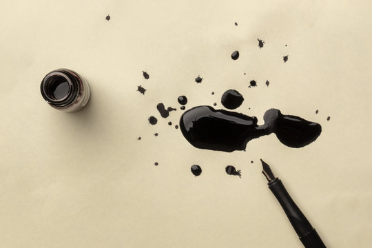 An overhead photo of an ink well with drops of ink and a nib pen, with copy space