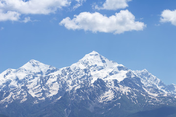 Fototapeta na wymiar Snowy mountain peak against a blue sky with white clouds. Mountain landscape of the rocky mountain.