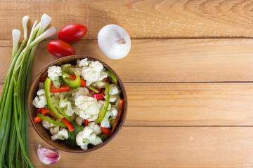 Fresh salad of cauliflower with tomatoes, broccoli, olives, sweet pepper, herbs and vegetables in a bowl on a wooden table. Top view. Copy space