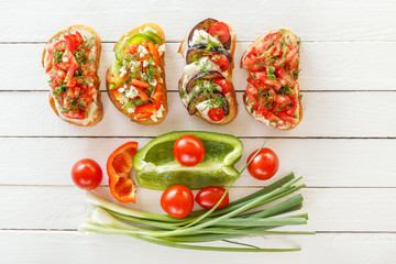 Bruschetta with fresh tomatoes and cheese, eggplant and mozzarella, sweet pepper and goat cheese on white boards with fresh vegetables. Top view.
