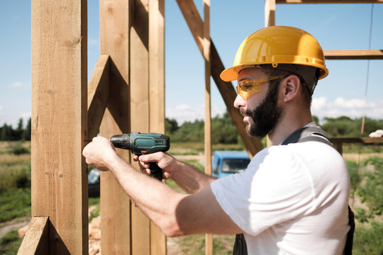 The man is a builder on the roof of a wooden frame house.