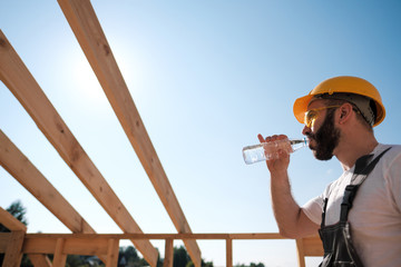 The man is a builder on the roof of a wooden frame house.
