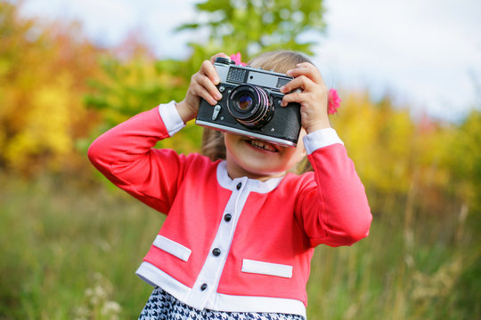 a little girl in a pink jacket and a black and white dress with two tails photographing an old camera