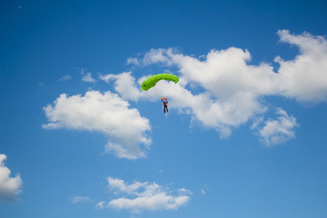 Man, a paratrooper is flying through the blue sky amidst white clouds on a parachute