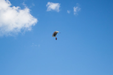 Man, a paratrooper is flying through the blue sky amidst white clouds on a parachute