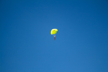 Man, a paratrooper is flying through the blue sky amidst white clouds on a parachute