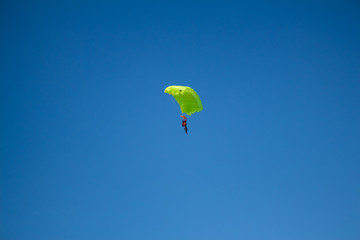Man, a paratrooper is flying through the blue sky amidst white clouds on a parachute