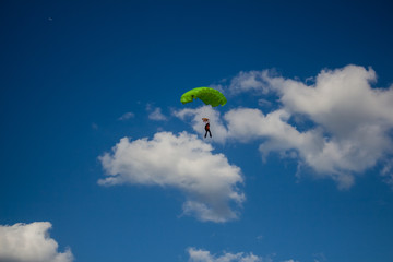 Man, a paratrooper is flying through the blue sky amidst white clouds on a parachute