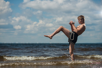 Fototapeta na wymiar Kickboxer kicks in the open air in summer against the sea.