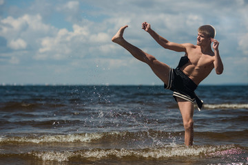 Fototapeta na wymiar Kickboxer kicks in the open air in summer against the sea.