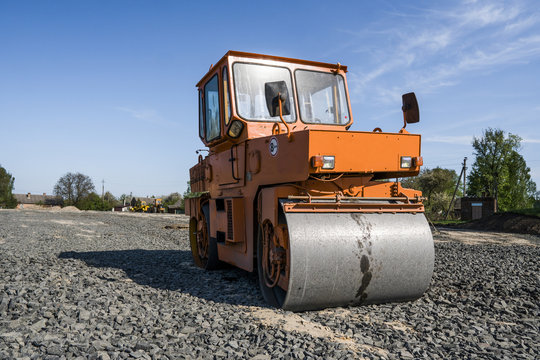 Orange light Vibration roller compactor standing on a stones at road construction and repairing asphalt pavement works with a blue sky.