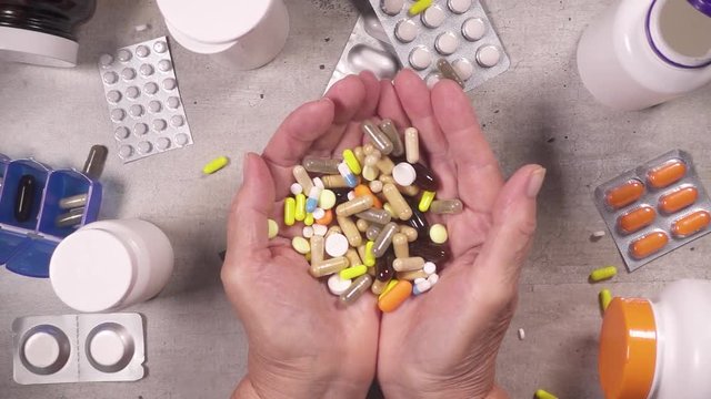 Slow motion on the table are scattered pills and bottles and a bunch of pills falls on the old open palm top view