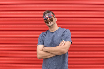 Fashionable man with three different kinds of sunglasses on red background