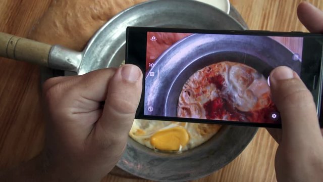 Taking Mobile Photo of Shakshuka Poached Eggs with Tomato and Bread Served in a Frying Pan. Israeli Arab Middle Eastern Cuisine. Top View