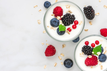 healthy yogurt with fresh forest berries in glasses on white marble background. healthy diet breakfast