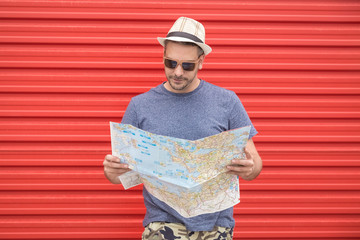 Fototapeta premium Portrait of hipster man holding map isolated on red metal wall. Travel concept.