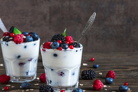 yogurt with fresh berries, oats and mint in glasses with spoons on rustic wooden background. healthy diet breakfast