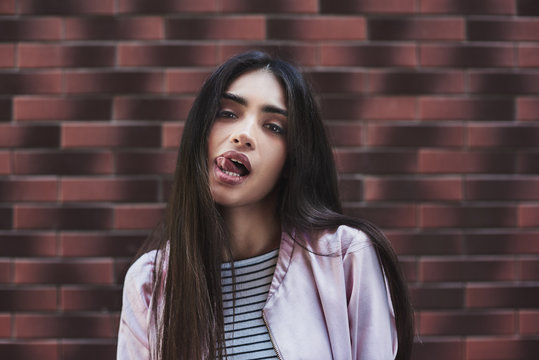 Young woman in pink jacket stading isolated on wall tongue out l