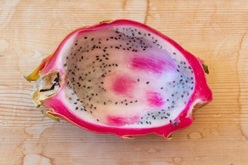 Close view of half of a dragon fruit with pulp spooned out, centered on weathered wood background,...