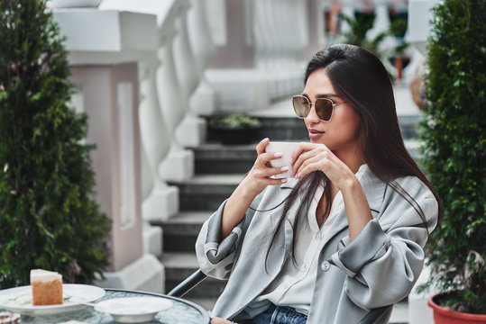 Young woman in sunglasses sitting at table in cafe ddrinking hot