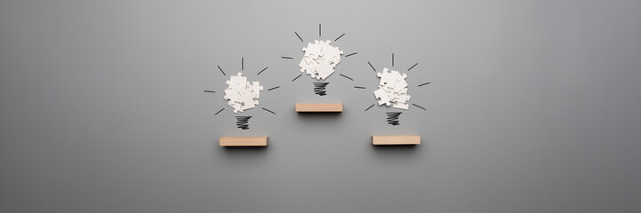 Wide panorama view of three light bulb formed by white puzzle pieces placed on wooden pegs