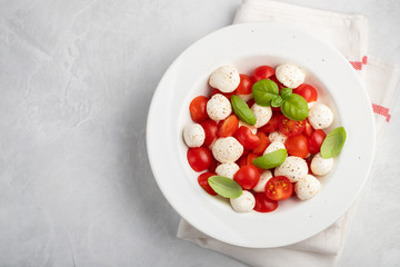 White plate of classic delicious caprese salad with ripe tomatoes, mozzarella and fresh basil leaves on gray background. copy space. Italian food. The concept of a healthy vegetarian diet. Top view