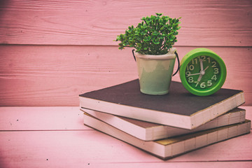 The abstract art design background of green alarm clock and ceramic pot with plant put on books stacked,on wooden timber board,vintage and art tone