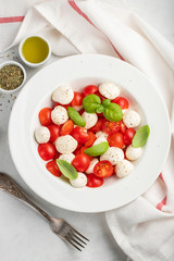White plate of classic delicious caprese salad with ripe tomatoes, mozzarella and fresh basil leaves on gray concrete background. Italian food. The concept of a healthy vegetarian diet. Top view