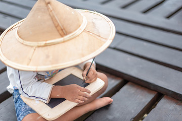 Little boy in Asian country pay attention on his writing. Child happy to learn. Happy boys getting a blackboard writing his name. Pre-school boy shows his hand writing outdoor.